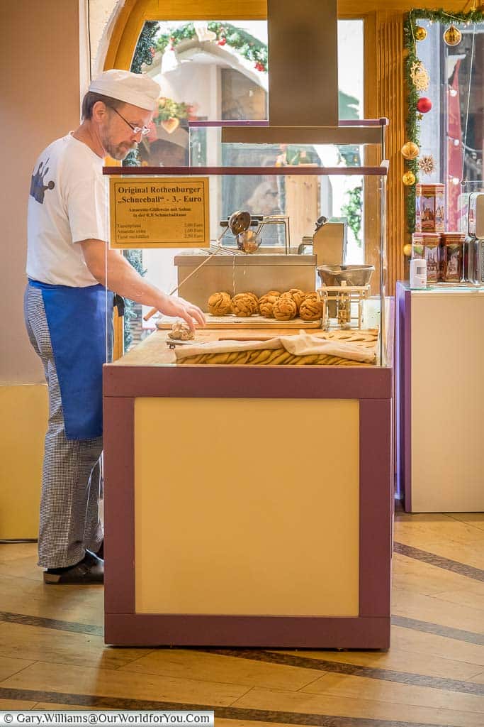 A man behind the counter in a cafe making fresh Schneeballen cakes