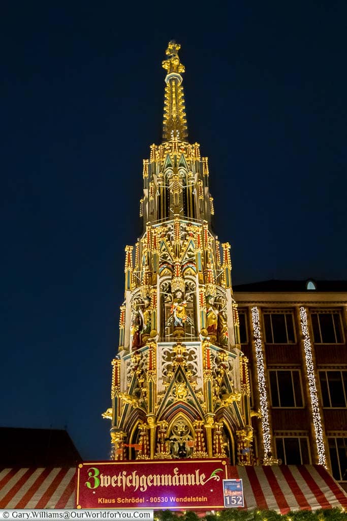 The tiered, ornately decorated Schöner Brunnen at night behind a stall in nuremberg's christmas market
