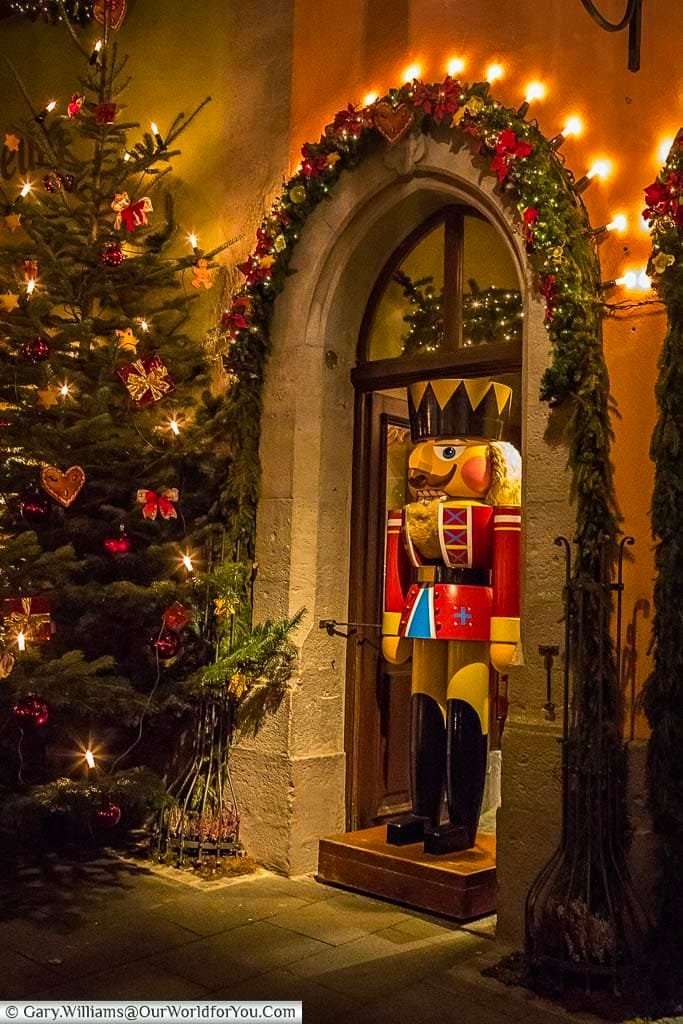 A lifesized soldier nutcracker stands in a decorated doorway of the Käthe Wohlfahrt store in Rothenburg ob der Tauber, next to a Christmas tree.