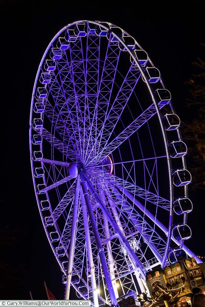 A large white modern ferris wheel illuminated in a blue/purple at night in one of düsseldorf's german christmas markets