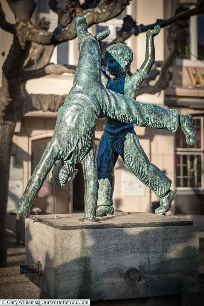 A bronze statue above a fountain of two children, one cartwheeling, in a symbol for düsseldorf in germany