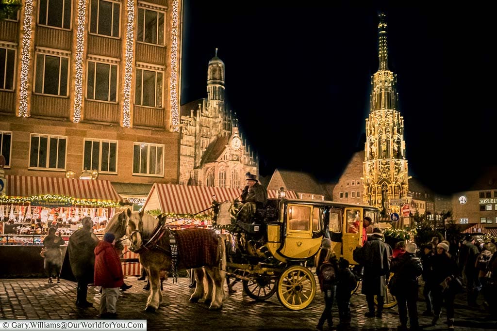 A traditional yellow & black carriage drawn by two horses in front of the Schöner Brunnen, a tall, ornate, lit gothic tower on top a fountain.