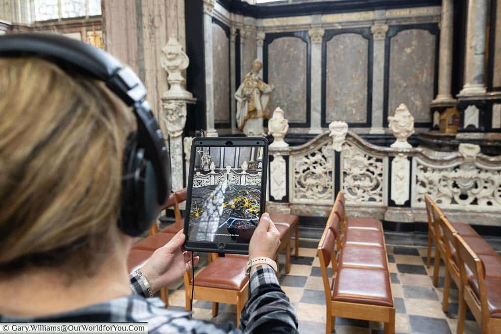 Janis holding a tablet in Saint Peter’s Church in Leuven displaying an augmented reality view of the city under fire in World war II