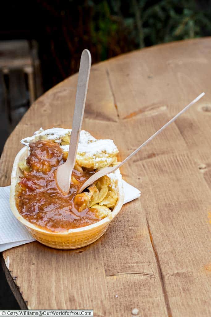 An edible bowl containing apple pancakes with lashings of plum sauce and two wooden forks.
