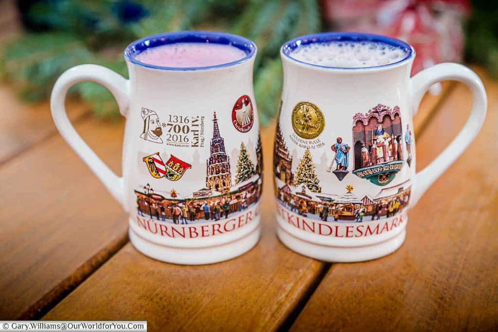 Two mugs of glühwein in the 2016 Nuremberg mugs. One is the regional version with added blueberries, and the other is a regular red version.