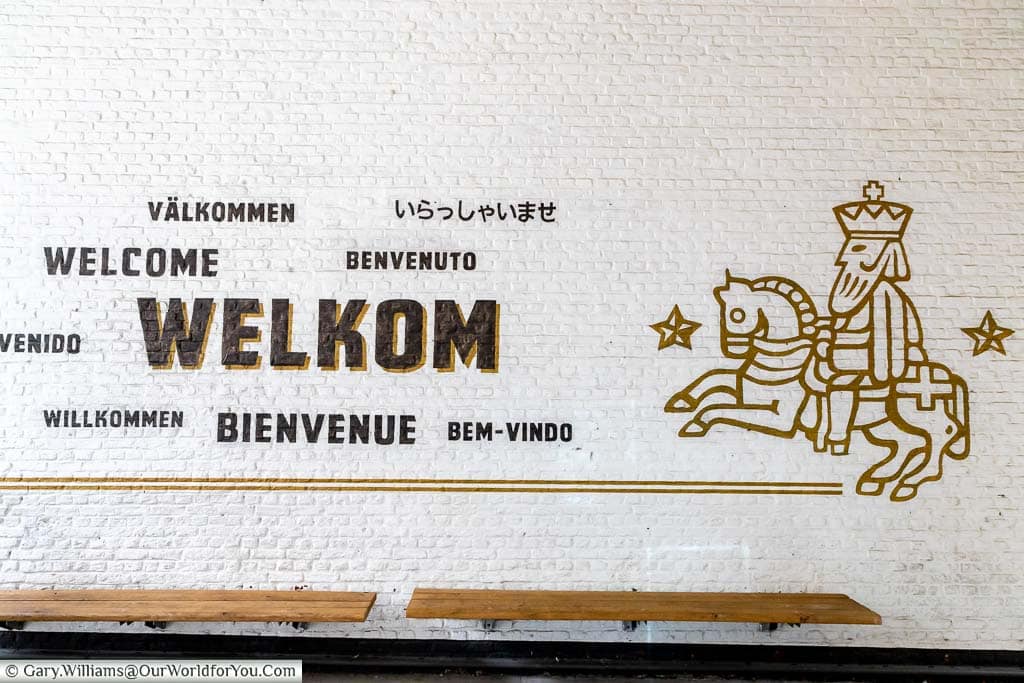 Welcome written in many different languages and the logo for the gouden carolus on a white wall at the entrance to the het anker brewery in mechelen