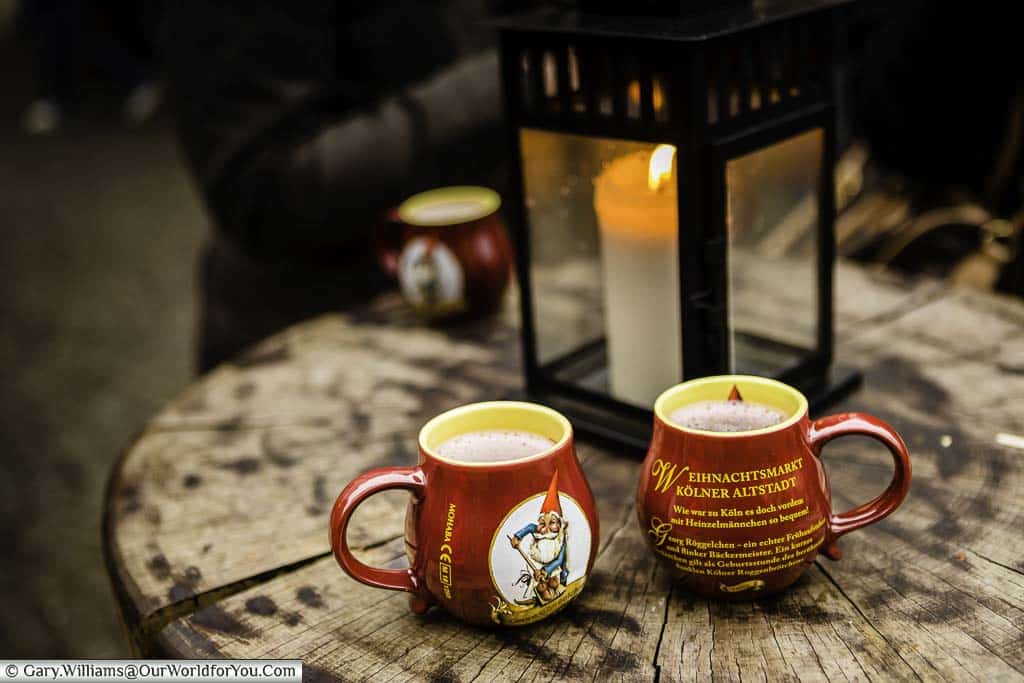 Two mugs of steaming glühwein in souvenir mugs on a table in front of a candle at the Christmas Markets in Cologne, Germany