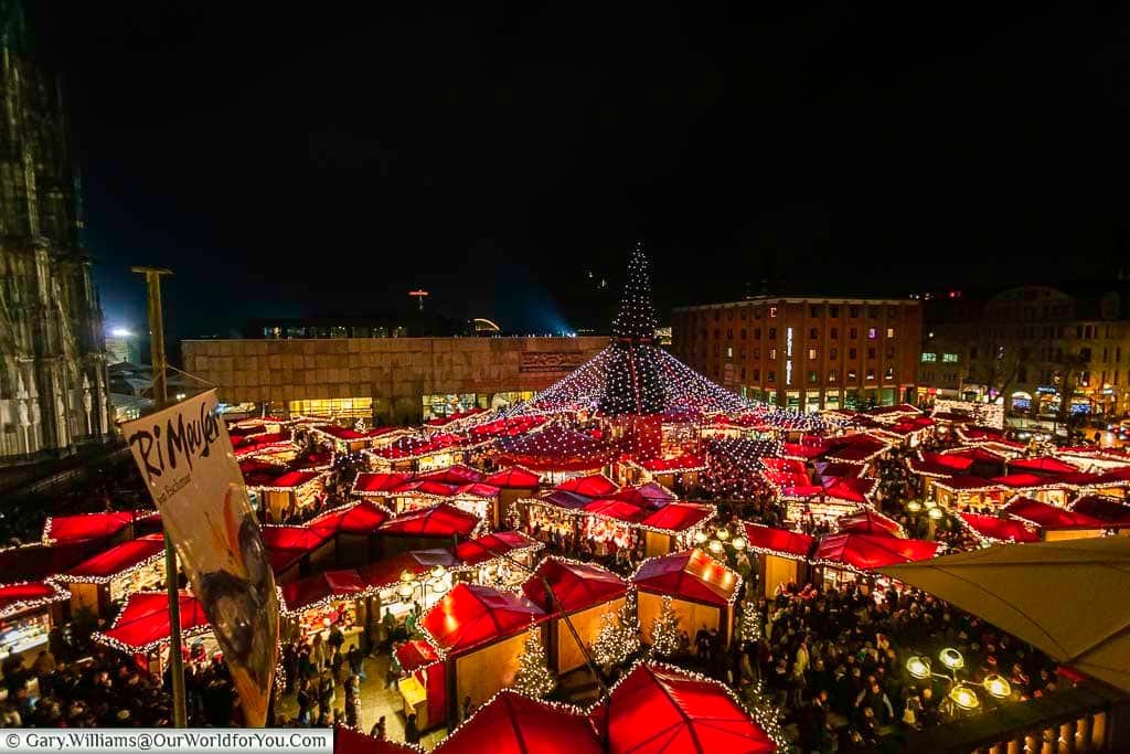 Looking over the red rood tops of the huts of cologne's dom christmas market at night with the central christmas tree and it's blanket of twinkling fairy lights