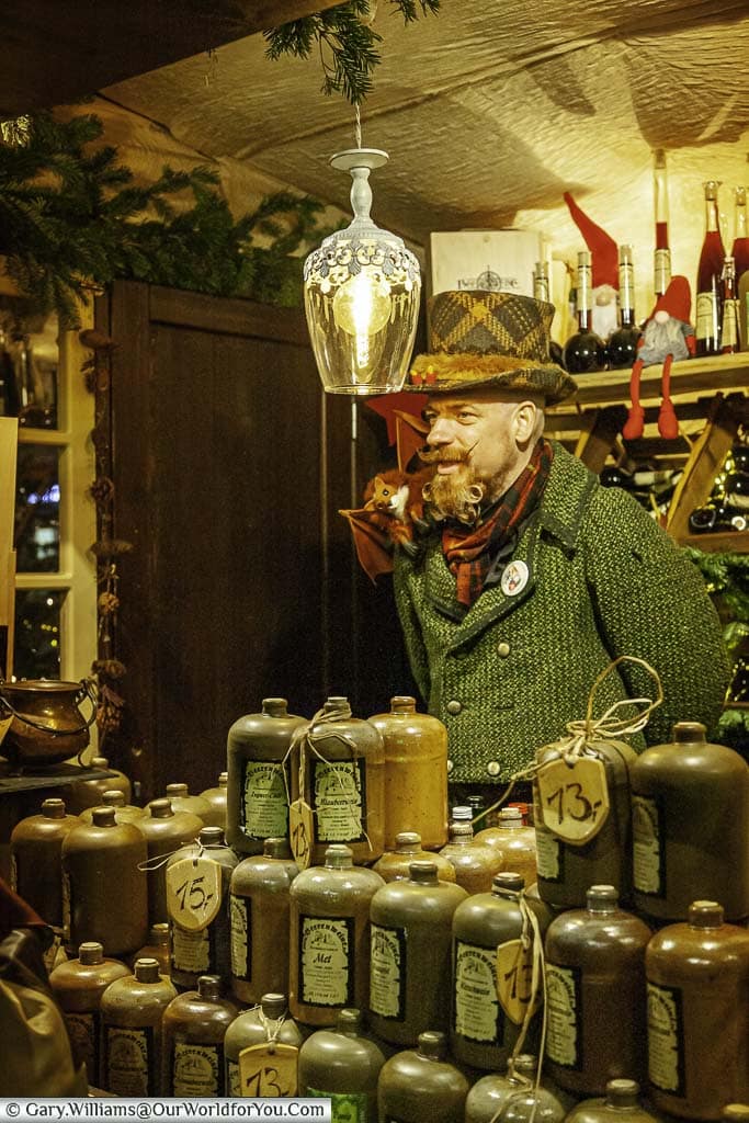 An intriguing figure of a man dressed in period clothes from the 18th century, sporting a manicured beard, selling berry wines in glazed stone containers on a colgne market stall in the old town