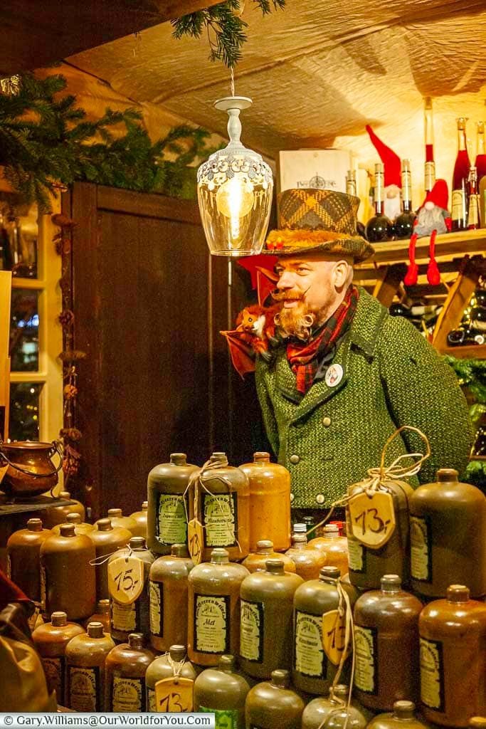 An intriguing figure of a man dressed in period clothes from the 18th century, sporting a manicured beard, selling berry wines in glazed stone containers on a colgne market stall in the old town