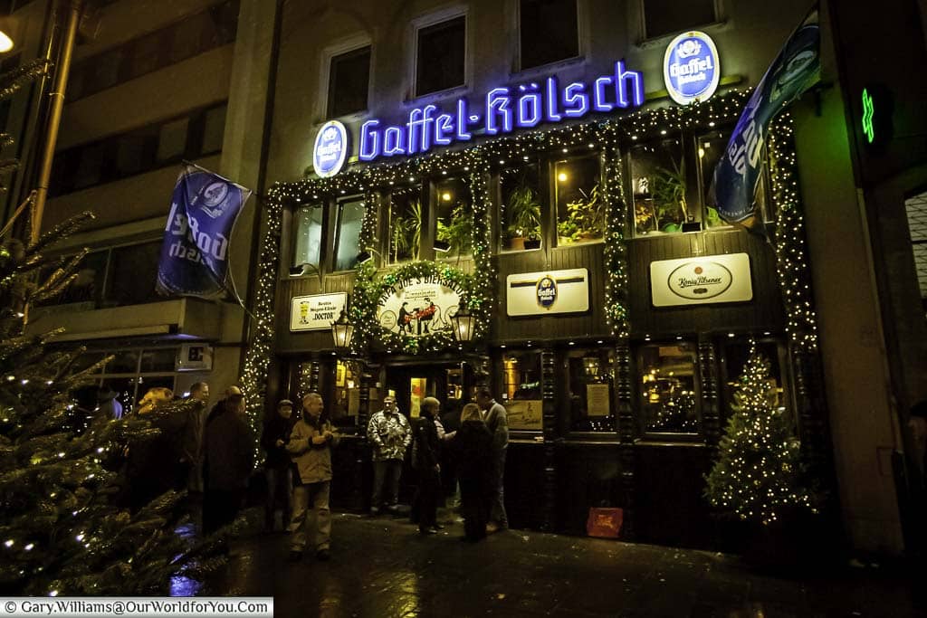 Outside Papa Joe's Biersalon In the evening. The pub is decorated with twinkle lights and sign displaying they serve Gaffel Kölsch.