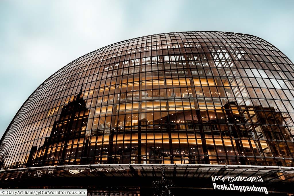 The old glass egg shaped Department store of Peek & Cloppenburg under dark grey winter sky. The scene is lit with a golden light coming from inside the store. It's one of the main Department stores in Cologne.