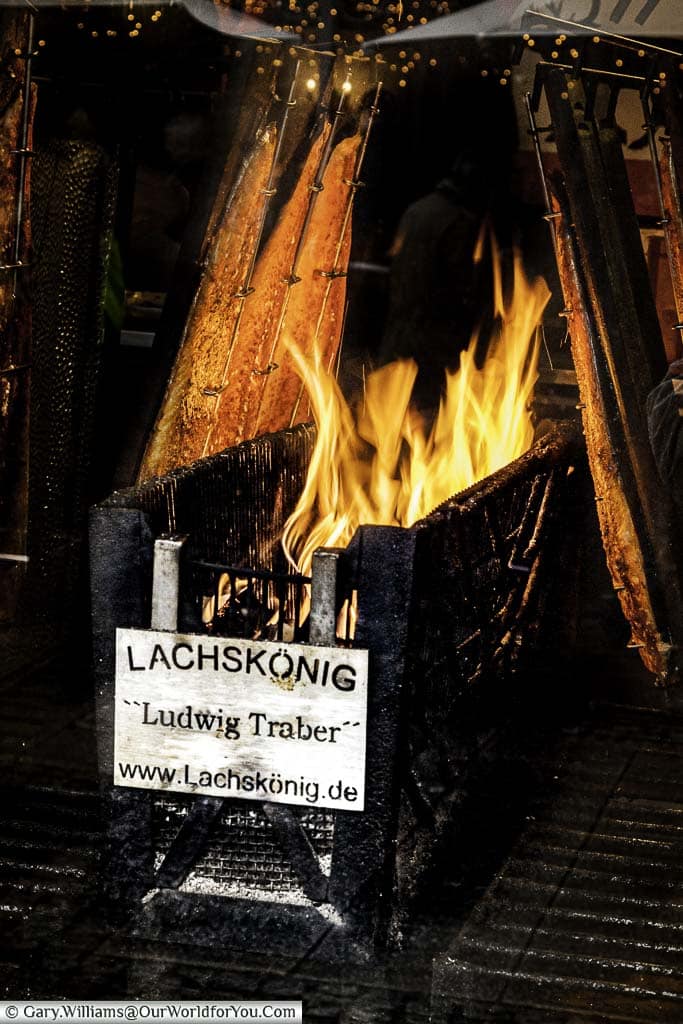 Salmon grilling next to a flaming wood fire for sale on the Cologne Christmas Markets