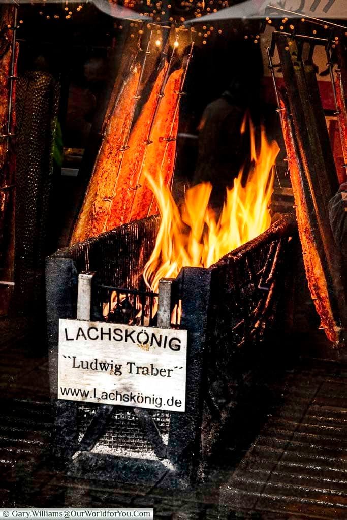 Salmon grilling next to a flaming wood fire for sale on the Cologne Christmas Markets