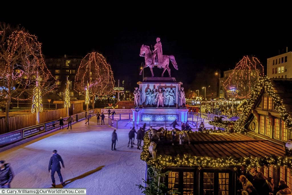 The Cologne ice rink from the bridge that straddles it, looking to the loop around the statue to Friedrich Wilhelm III on horseback. In the foreground to the right is a beautifully crafted and ornate cabin serving gluhwein.