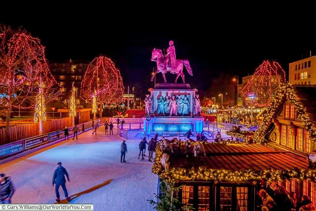 The Cologne ice rink from the bridge that straddles it, looking to the loop around the statue to Friedrich Wilhelm III on horseback. In the foreground to the right is a beautifully crafted and ornate cabin serving gluhwein.