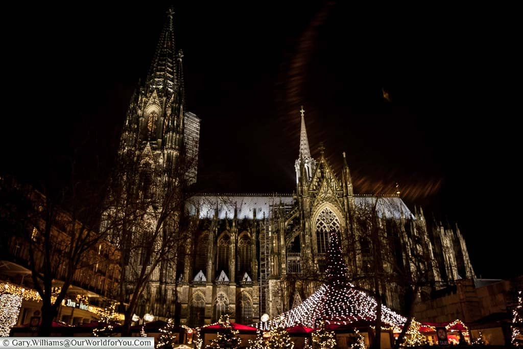 Looking up at the lit Dom Cathedral at night with the Christmas tree and its blanket of lights meeting the red-topped market huts.