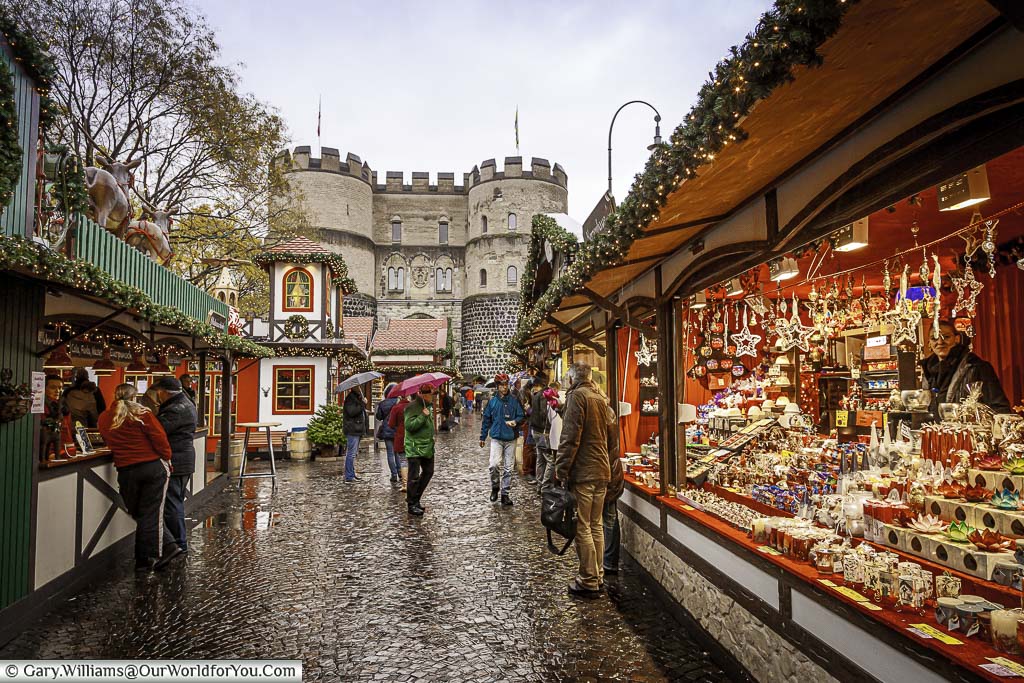A view of the historic Hahnentorburg gate from within a damp Village of St Nicholas Christmas market in Cologne.