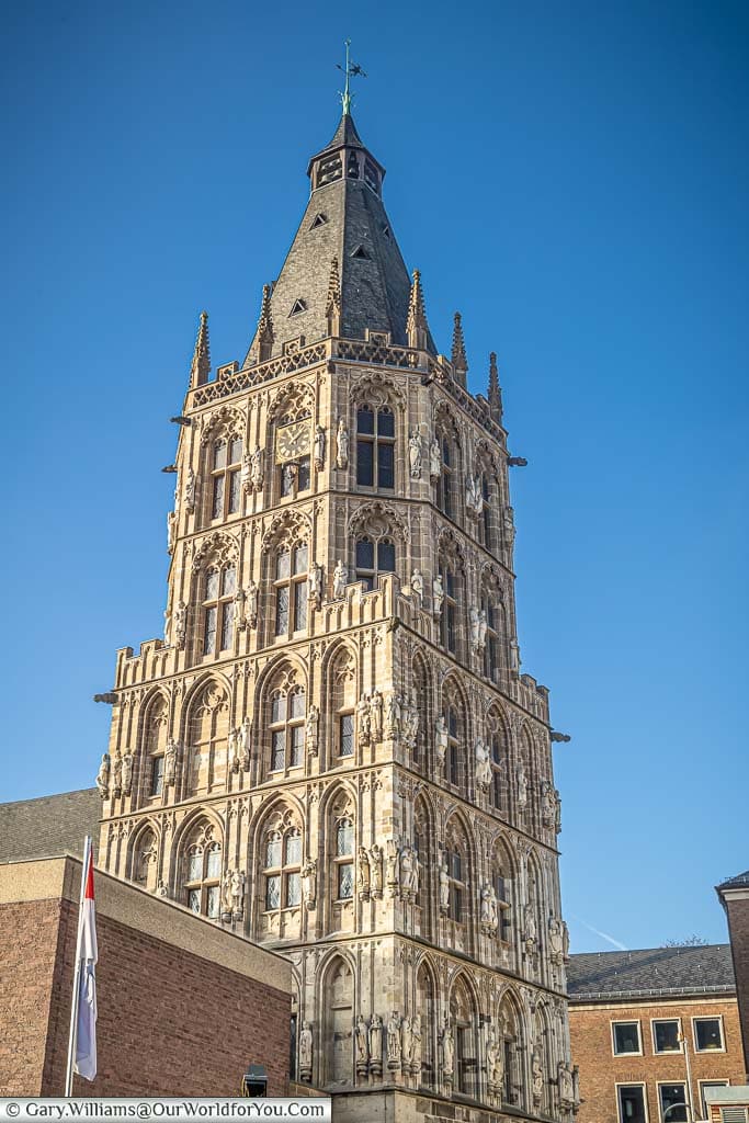 A portrait shot of the detailed gothic tower of Cologne’s Rathaus against a deep blue sky.