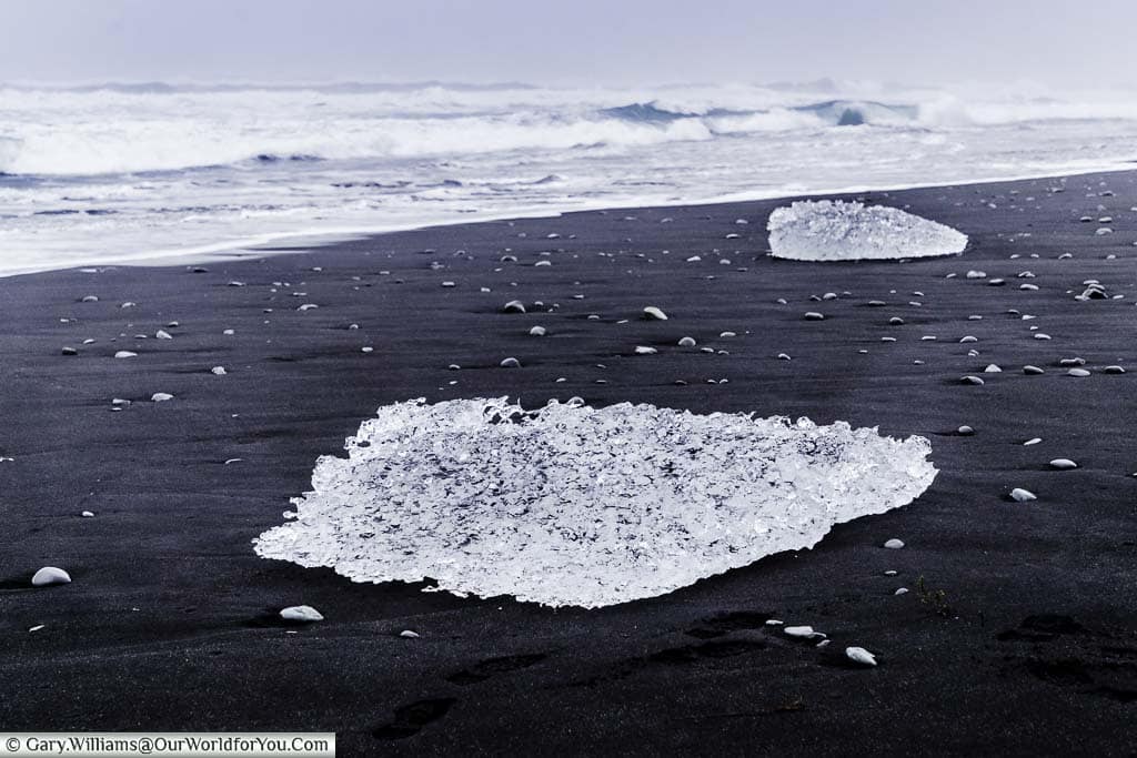 Lumps of crystal clear ice washed up on the jet black sand of Diamond Beach with the rolling waves in the background.