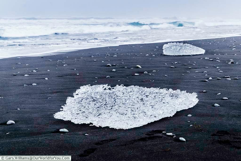 Lumps of crystal clear ice washed up on the jet black sand of Diamond Beach with the rolling waves in the background.