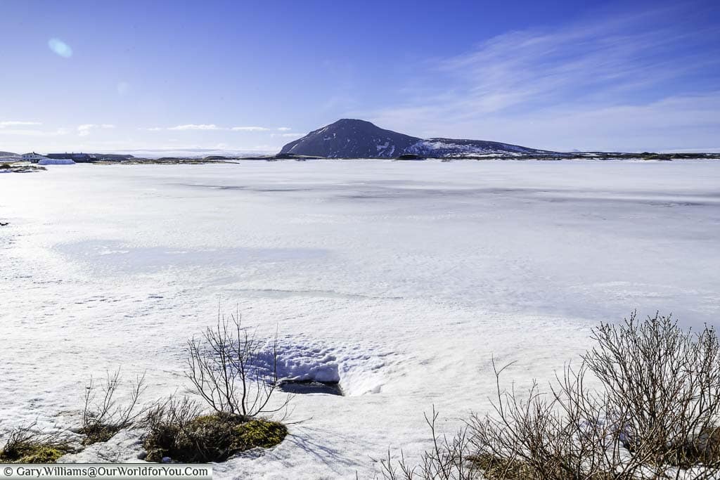 A frozen section of Lake Myvatn in Iceland with a lone mountain in the background