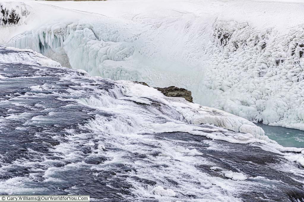 A close-up of the foaming blue waters falling into the ice-covered ravine of the Gullfoss waterfall on Iceland's golden circle
