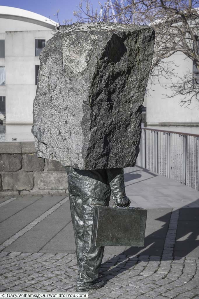 A bronze statue of an office worker in trousers, holding a briefcase set in a rectangular stone block from the tourso up in the centre of reykjavik, iceland