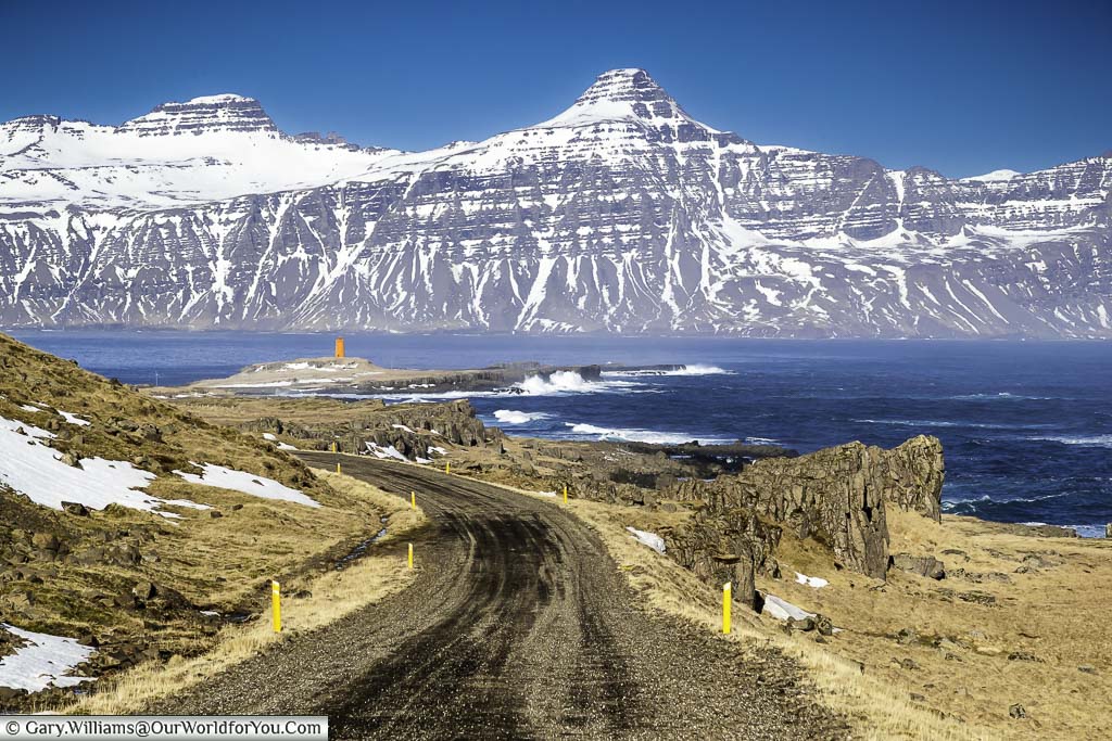 The gravel route 955 leading towards a lighthouse against a backdrop of Icelandic mountains