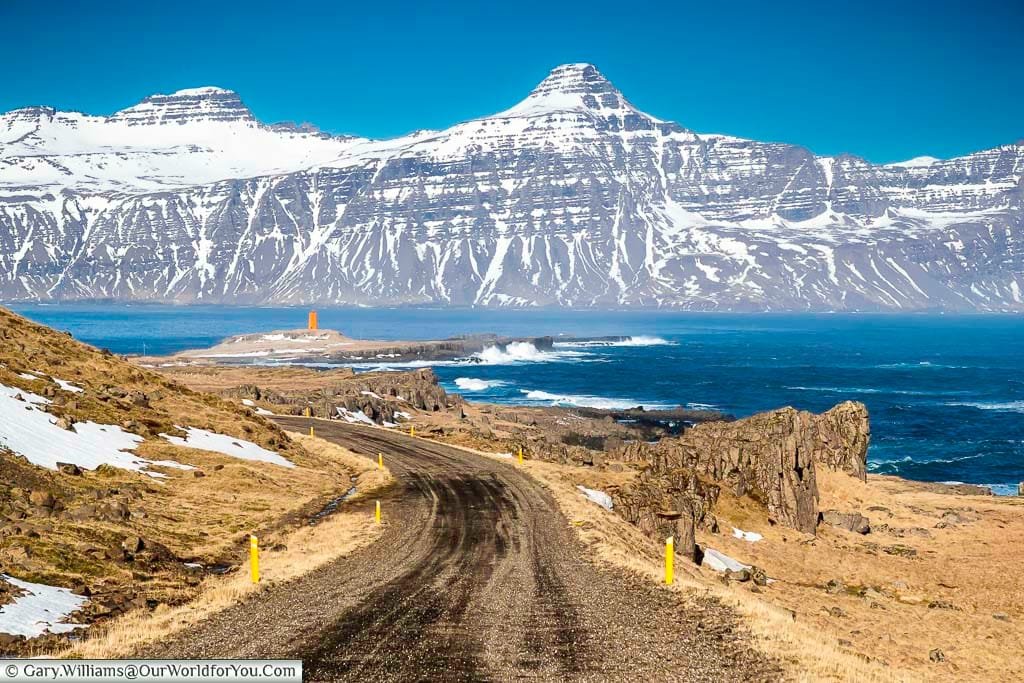 The gravel route 955 leading towards a lighthouse against a backdrop of Icelandic mountains