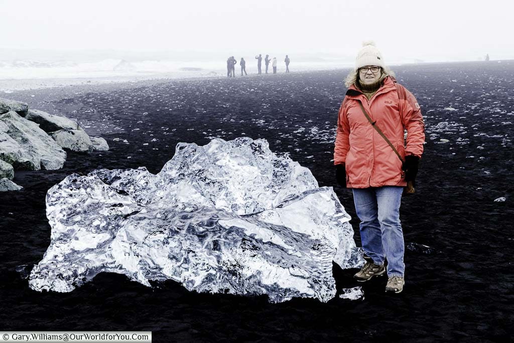 Janis standing next to a lump of crystal clear ice washed up on the jet black sand of Diamond Beach