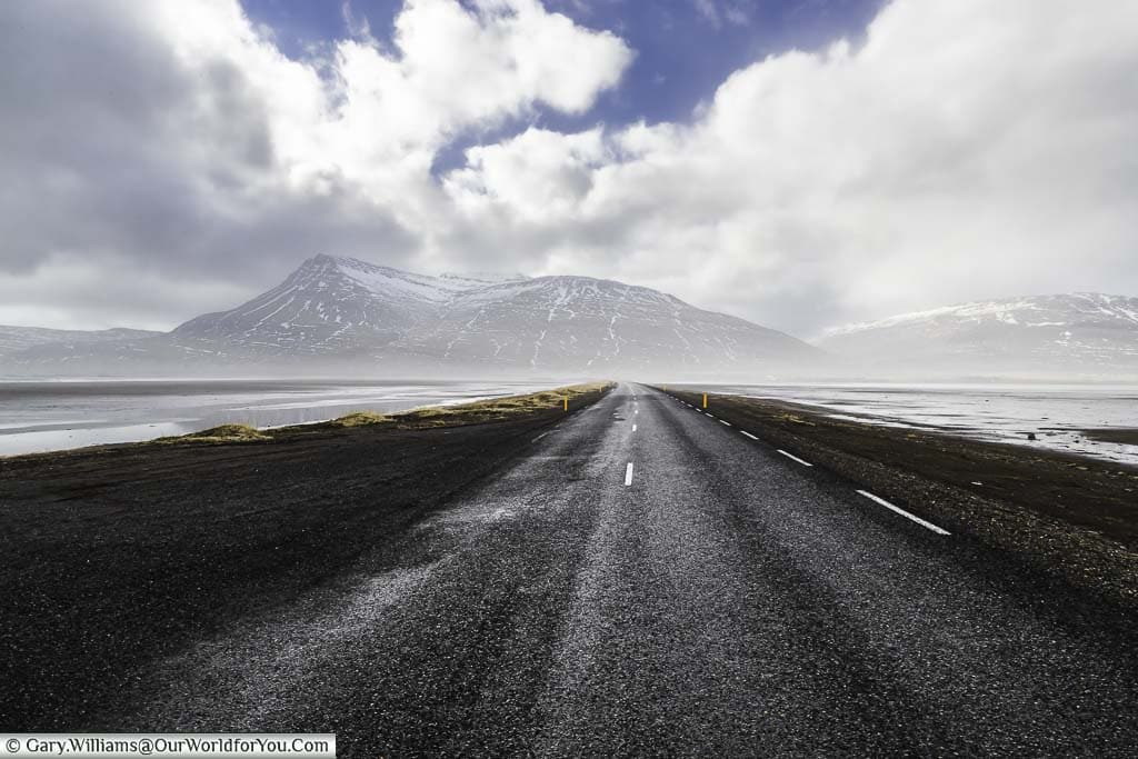 Iceland's route one crossing a spit of land, with water on both sides, towards ice-capped mountains