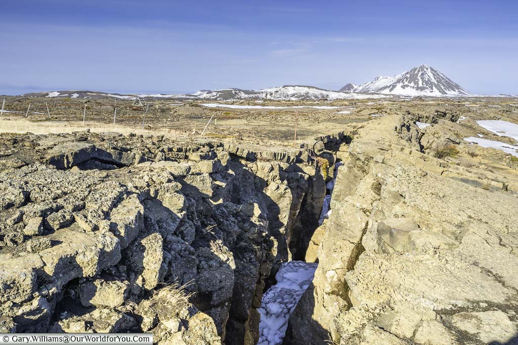 A fissure in the rocky landscape of Iceland with a snow-capped mountain the the background