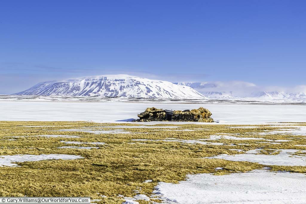 A turfed shack on the edge of the frozen Svartárvatn lake in Iceland with snow-covered mountains in the background