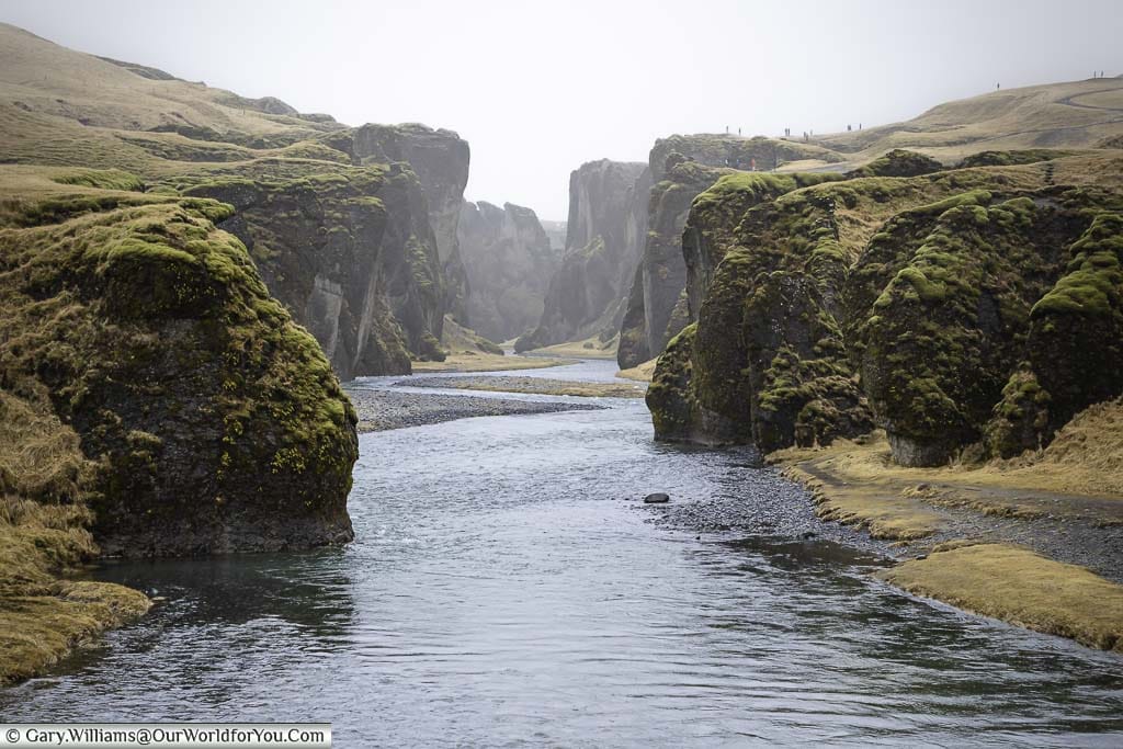 Icy blue/black water meanders along the misty Fjaðrárgljúfur Gorge in Iceland
