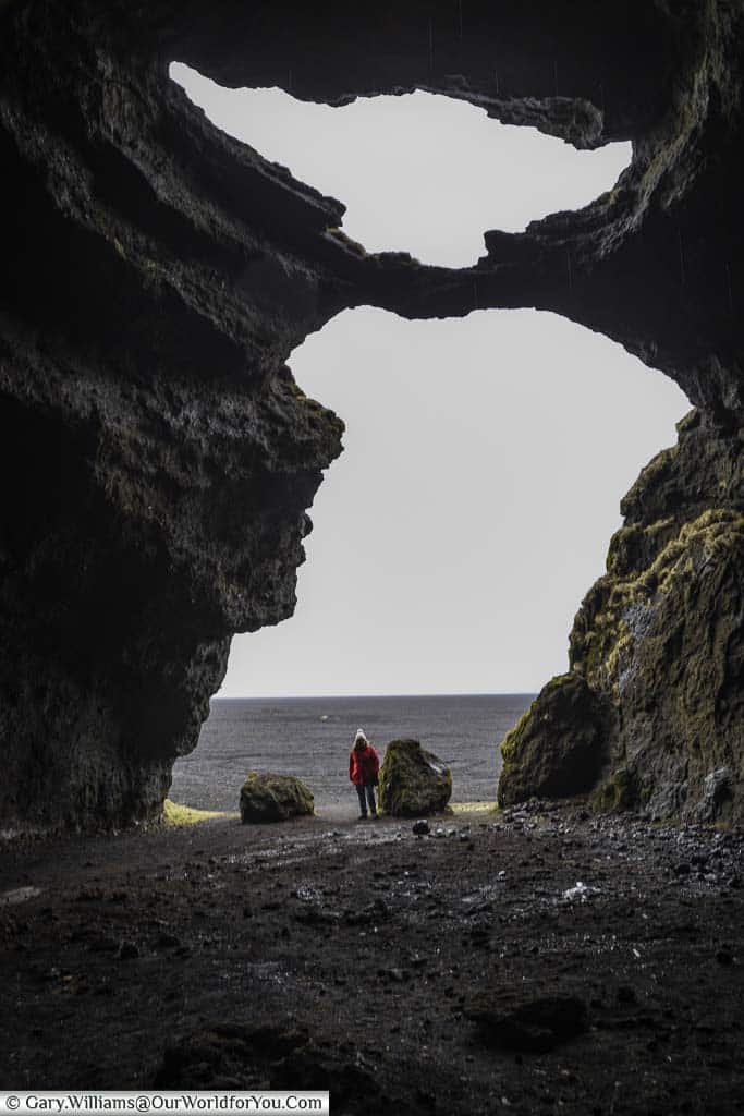 The view from the back of the Hjörleifshöfði Cave with Janis dwarfed with the gigantic entrance as she looks out to beyond