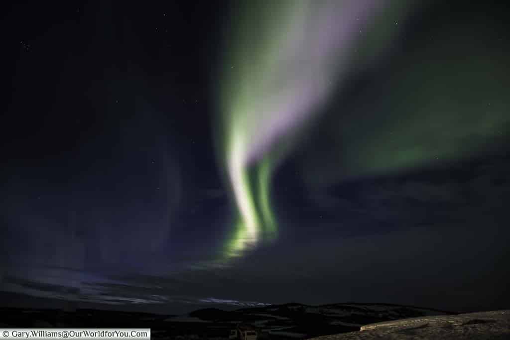 Two streaks of pale green and purple light of the Northern lights over the landscape of Reykjahlíð in Eastern Iceland