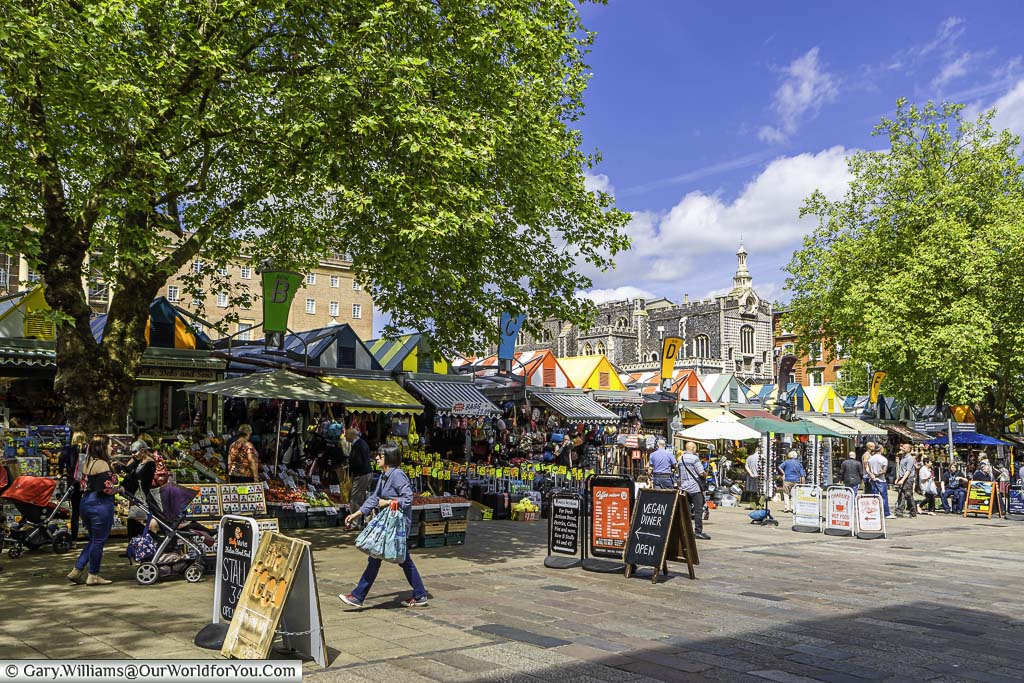 The bustling Norwich Market, with its brightly topped stalls, on a beautiful spring day.