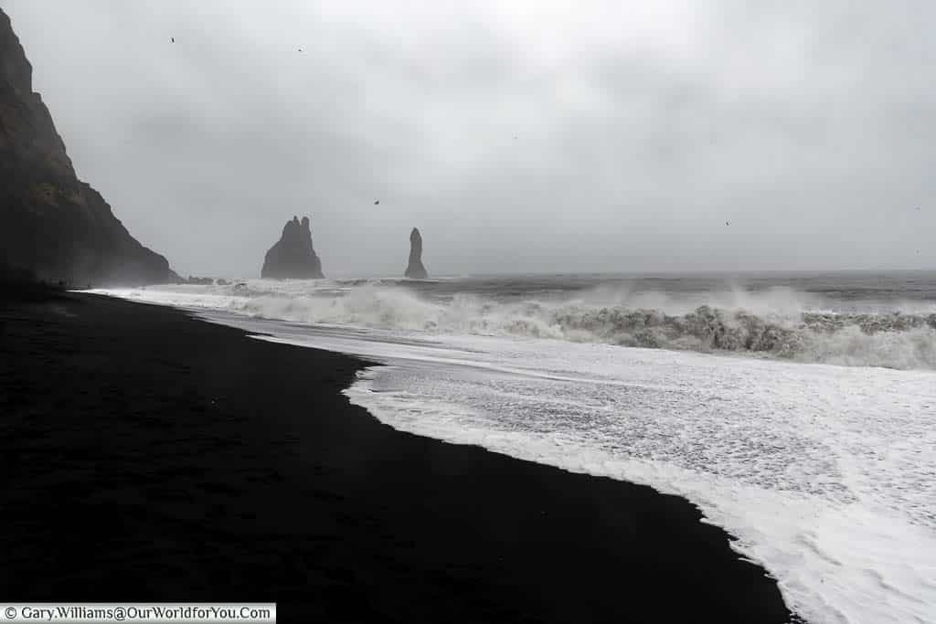 Waves breaking on the Reynisfjara Beach on a stormy day with Basalt Rock pillars in the background