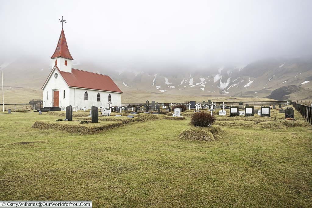 The red-topped white Reyniskirkja church and graveyard in Vik with the mountains at the rear covered in mist
