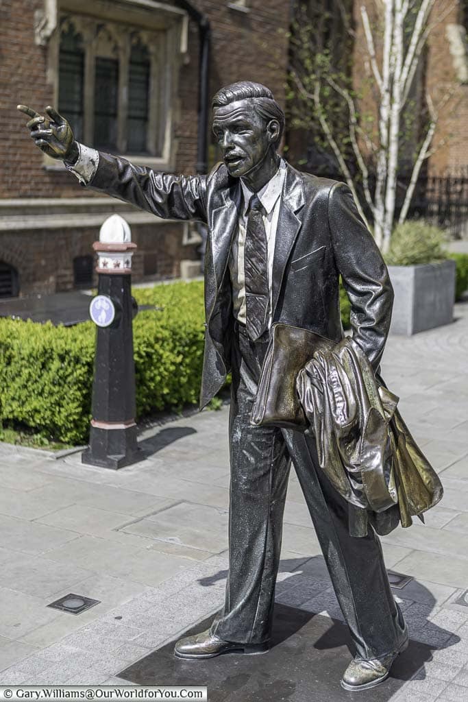 A bronze statue to a suited London city worker hailing a taxi.