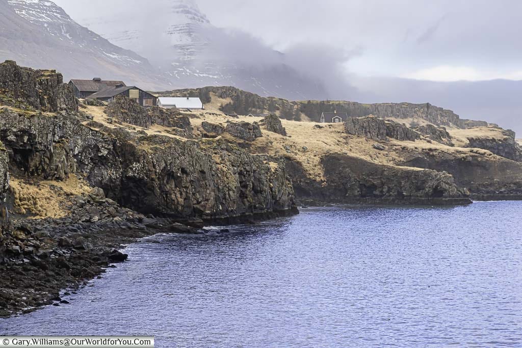 Isolated homes perched on a rocky landscape next to a fjord in Eastern Iceland