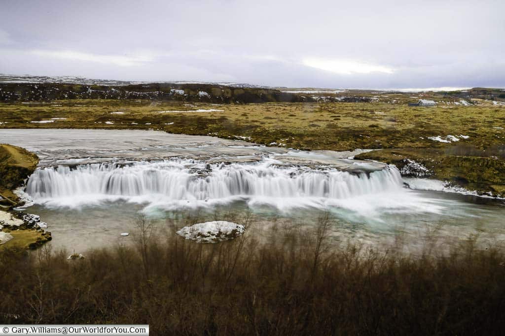The blurred white water flowing over the Faxi waterfall against a thawed bleak backdrop in Iceland