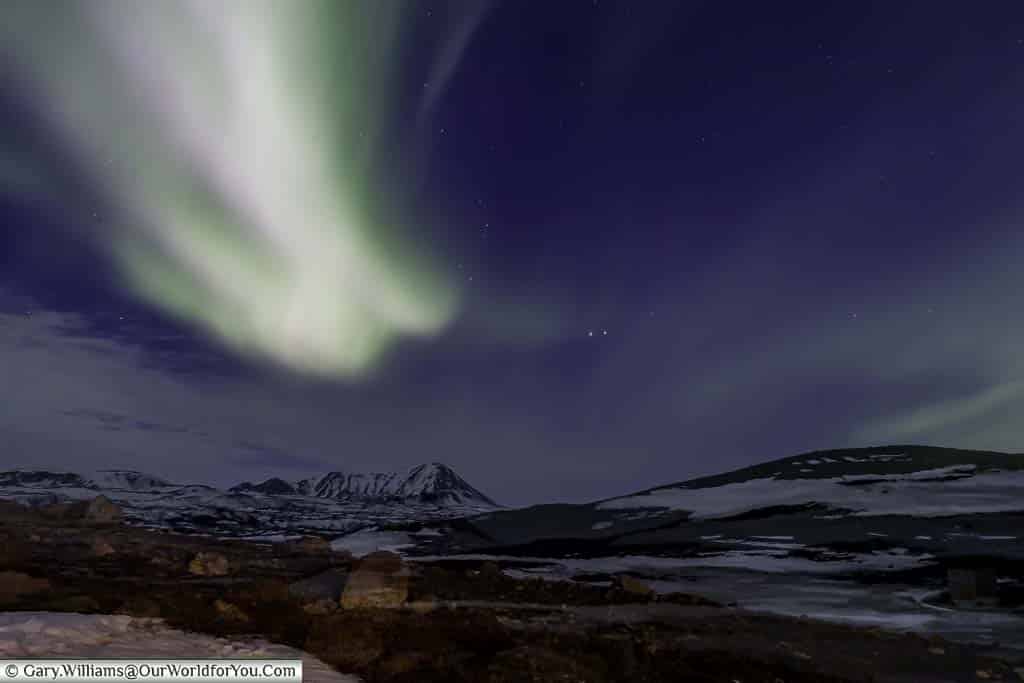 Streaks of pale green light of the Northern lights over the baron landscape of Reykjahlíð in Eastern Iceland