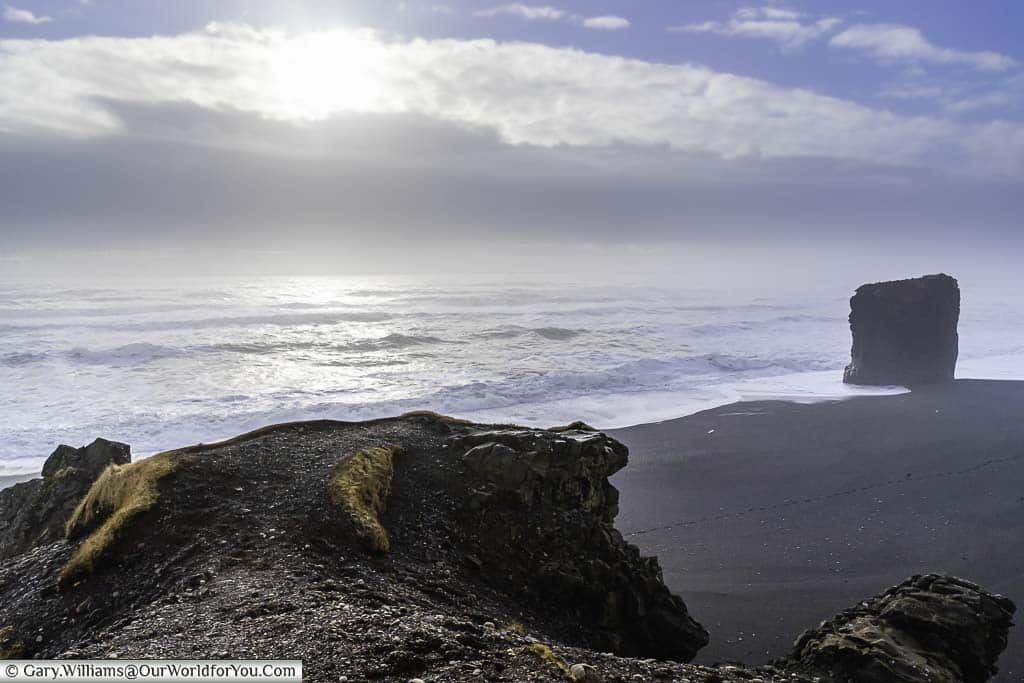 A lone rock pillar on a black beach in eastern Iceland on a bright day