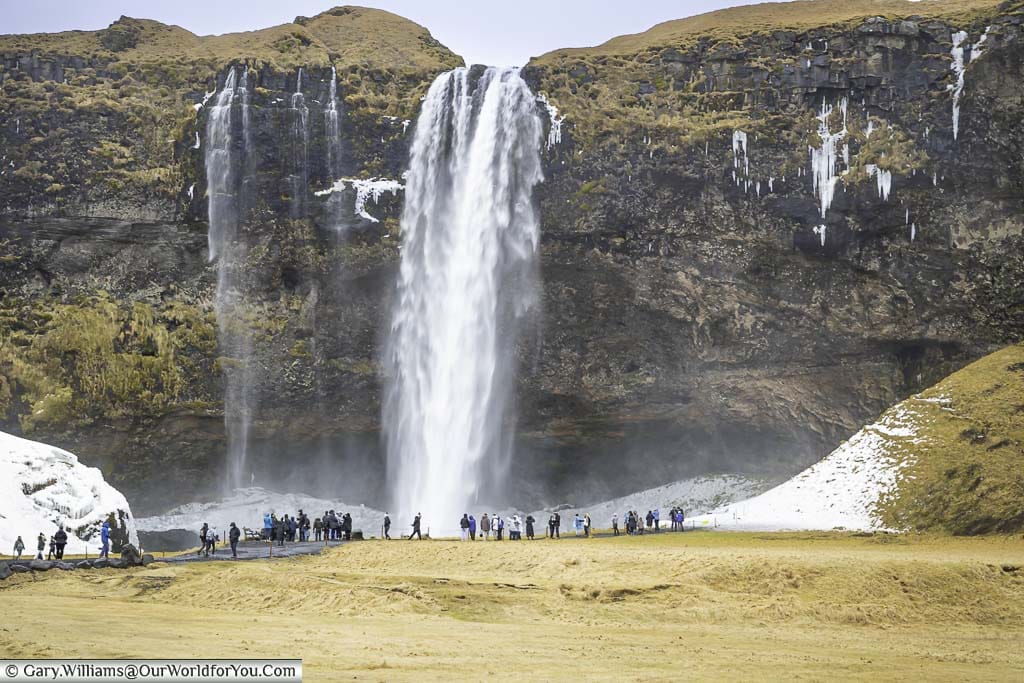 A small group of people in front of the Seljalandsfoss waterfall as seen from a distance.