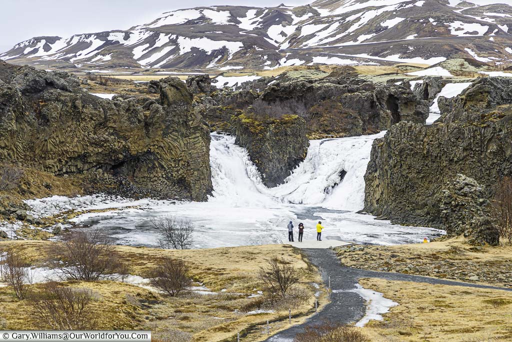 A small group in front of the twin frozen falls of Hjálparfoss surrounded by a basalt rock formations