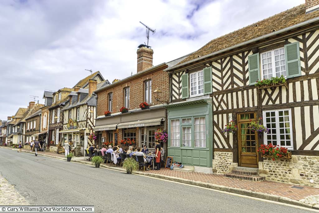 The high street in Beuvron-en-Auge with half-timbered homes, shuttered windows and tables & chairs outside a café