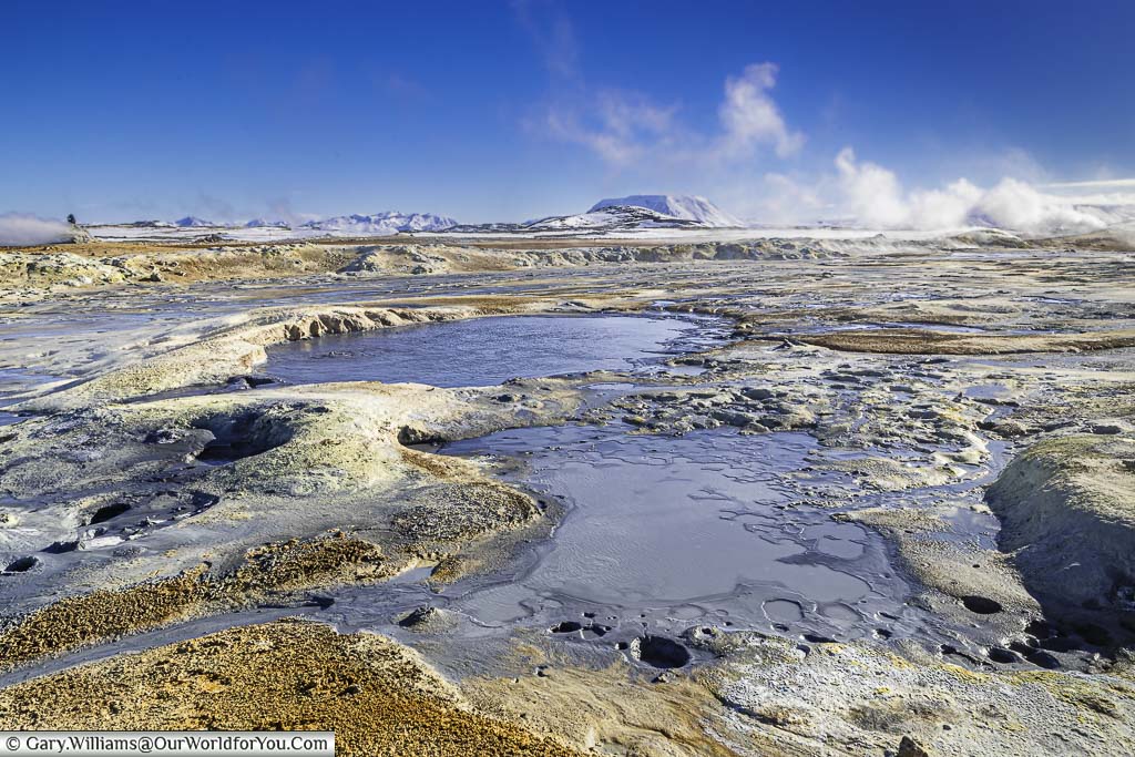 Dark grey mud pools bubble between sulfur stained rock at the geothermal park of Námafjall Hverir in Iceland