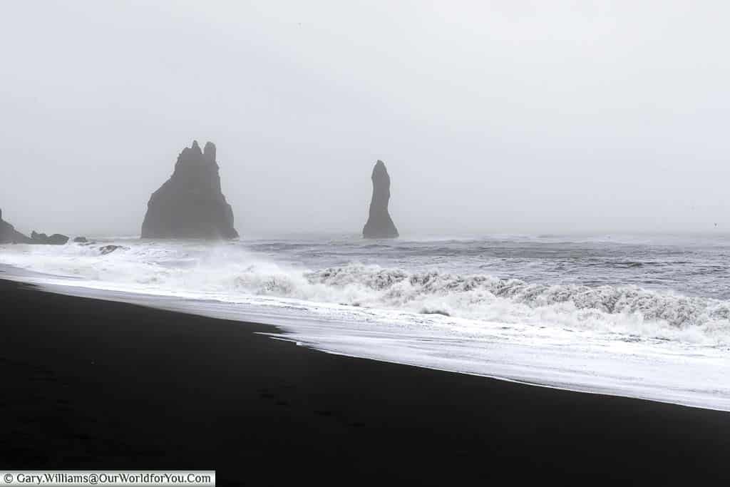 Waves breaking on the Reynisfjara Beach on a stormy day with Basalt Rock pillars in the background